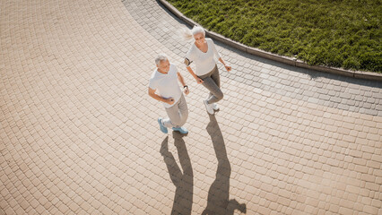 Top angle view of sporty healthy active elderly couple man and woman running jogging going to workout outdoors in green park. Sports healthy lifestyle for retired people. Friends on a morning walk.