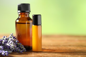 Bottles of lavender essential oil and flowers on wooden table, closeup. Space for text