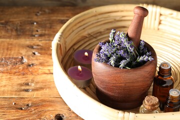 Bottles of lavender essential oil, burning candles and flowers on wooden table, closeup. Space for...