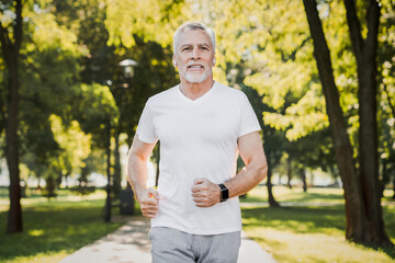 Senior man running in a park with a smile on his face and earphones on. Elderly man embracing...