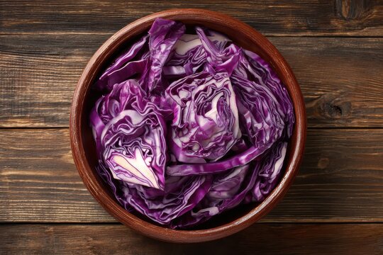 Raw red cabbage slices in a ceramic bowl on a rustic wooden table seen from above