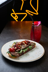 Gourmet beef bruschetta with cocktail in neon bar