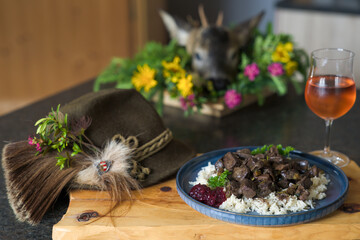 happy hunting of a young roe buck - fresh innards from a roe buck hunt, roasted with herbs, rice and cranberries, served on a blue plate and a glass of wine, decorated with the hunting hat