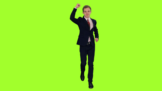 Young elegant businessman in suit giving hand up in a gesture of victory while walking on green chroma key background
