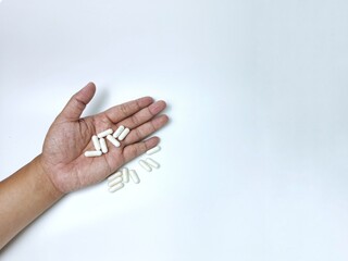 Hand holding white medicine capsules on white