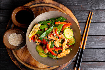 Asian food stir fried green peas with chicken and vegetables, sesame seeds in a bowl top view