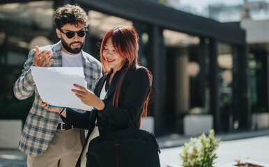 Two business colleagues review documents together while standing outside on a bright day.