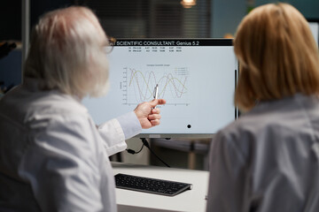 Senior Caucasian man and middle aged Caucasian woman analyzing scientific graph on computer monitor...