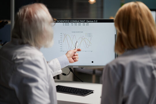 Senior Caucasian man and middle aged Caucasian woman analyzing scientific graph on computer monitor in laboratory, man pointing at data with pen while discussing research findings