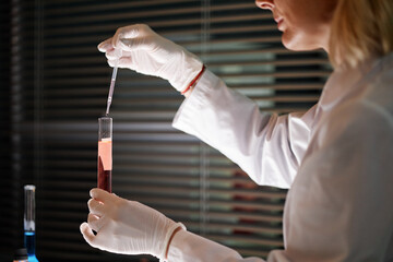 Caucasian middle aged woman wearing gloves conducting experiment in scientific laboratory, holding...
