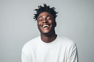 Studio portrait of a young Black African American male model with curly dreadlocks, laughing against a neutral grey backdrop. Casual white sweatshirt, cheerful, vibrant, and carefree vibe.