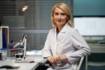 Portrait of middle aged Caucasian woman scientist smiling at camera while sitting at laboratory...