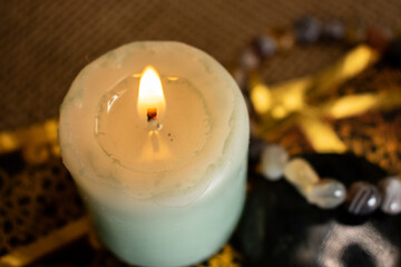 A green candle glows beside an agate bracelet and labradorite on ornate black and gold cards. Set on burlap, the scene evokes mysticism, ritual, and spiritual symbolism.