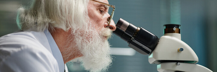 Website header shot of senior Caucasian man examining specimen using laboratory microscope,...