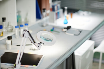 Laboratory table displaying scientific glassware, magnifying lamp, notebook, and laboratory...