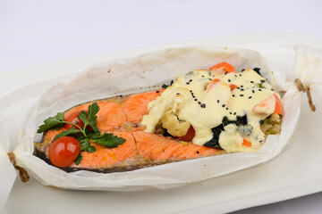 
baked salmon fillet with sauce in parchment on a white background