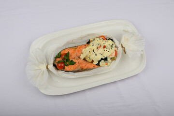 baked salmon fillet with sauce in parchment on a white background with decor