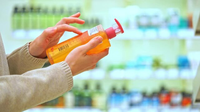 Woman holding a bottle of shampoo or body wash in a beauty store, reading the label, examining ingredients. Close-up of female hands. Concept of conscious choice, haircare, personal skincare awareness