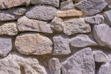 Ancient castle wall made of various sized grey and beige stones, forming a rustic textured background, suitable for historical tourism, architectural preservation, and building material suppliers