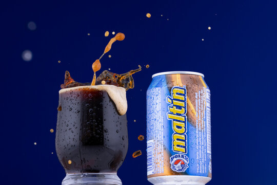 Venezuelan Malt&iacute;n Polar can next to a glass with the cold beverage with a splash, showing foam and droplets. Classic non-alcoholic malt beverage served cold.