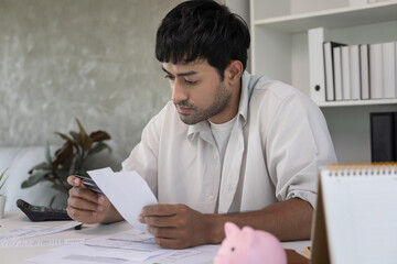 Stressed and headache asian man with large bills or invoices no money to pay to expenses and credit...