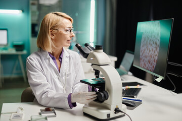 Caucasian middle aged female scientist examining biological samples under microscope while...