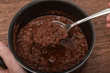 A confectioner stirring a pot with a spoon spoiled chocolate dessert icing for cakes, an accident at work, spoiled chocolate
