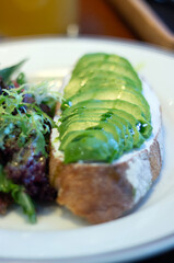 avocado toast with cream cheese and some salad on the side served in a white plate