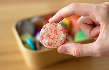 hand holding a disc of compressed chinese tea with a box of different types of teas on the...