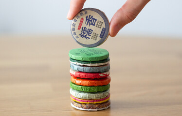 hand taking a disc of compressed chinese tea from a column of similar round tea bricks, isolated