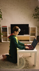 Study in slippers. Young boy in a dinosaur onesie works on coding at a low table, focused on his...
