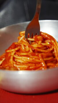 A person is eating spaghetti with meatballs. The spaghetti is in a bowl and the meatballs are in the middle of the spaghetti