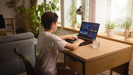 Focused boy working on digital analytics dashboard on a laptop in a cozy, well-lit home setting....