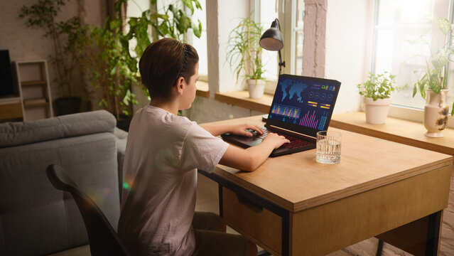 Focused boy working on digital analytics dashboard on a laptop in a cozy, well-lit home setting. Concept of early digital skills, data visualization and home-based education