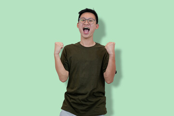 Excited Young Man Celebrating Success with Raised Fists on a Pastel Green Background