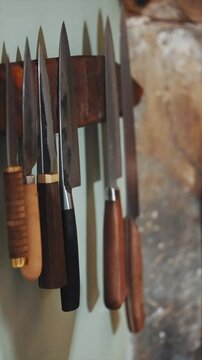 A wooden knife rack with a variety of knives hanging from it. The knives are of different sizes and shapes, and they are all made of wood. Scene is rustic and natural