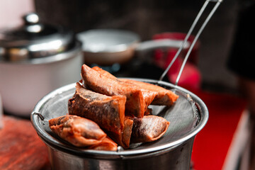 Crispy golden spring rolls draining oil on a metal strainer in a home kitchen setting. Perfect for culinary, Asian food, or cooking themes.