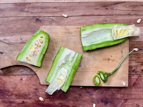 several pieces of bitter melon that are split and the inside is visible, scattered on a wooden cutting board isolated on a wooden table, bitter melon can be eaten directly or cooked first