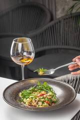 A gourmet serving of gnocchi with mushrooms, sun-dried tomatoes, parmesan, and fresh arugula, paired with a glass of white wine in an elegant dining setting
