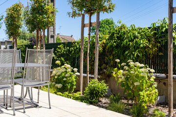 Jardin paysager am&eacute;nag&eacute; par une entreprise sp&eacute;cialis&eacute;e, avec pelouse, massifs fleuris, arbustes d&eacute;coratifs et mobilier de jardin &eacute;l&eacute;gant am&eacute;nag&eacute; sur une terrasse.