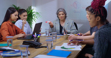 Indian young adult woman group sitting around table desk chair with boss CEO lady talk gossip enjoy work day indoor office female girl staff team group speak share good news spend break time job place