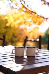 Cozy picnic in autumn forest. Camping coffee cups on wooden table at nature. Warm drinks in...