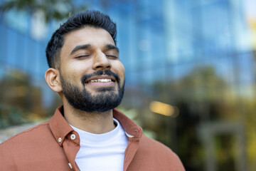 Close-up shot of a smiling Indian man with his eyes closed, seemingly enjoying a moment outdoors,...