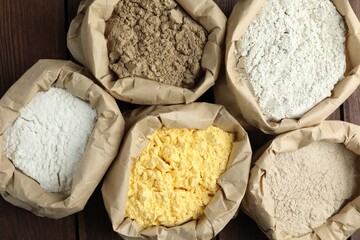 Different types of flour in paper bags on wooden table, flat lay