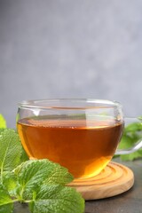 Aromatic lemon balm tea in glass cup and fresh leaves on gray table, closeup. Space for text