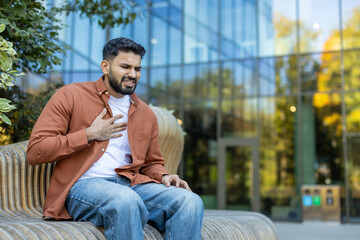 A man experiencing chest pain, sitting outdoors, likely having a health issue or heart attack, in a...