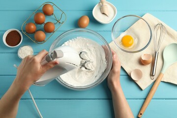 Woman whisking cream with hand mixer at light blue wooden table, top view