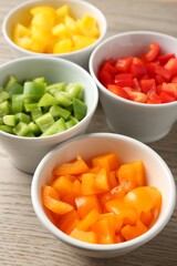 Pieces of fresh colorful bell peppers in bowls on wooden table, closeup
