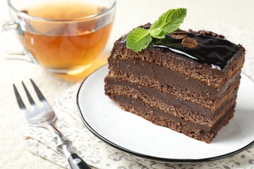 Piece of chocolate cake served with mint, fork and tea on table, closeup