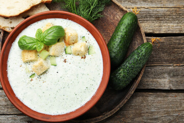 Tasty cucumber soup with croutons, basil, bread and vegetables on wooden table, flat lay